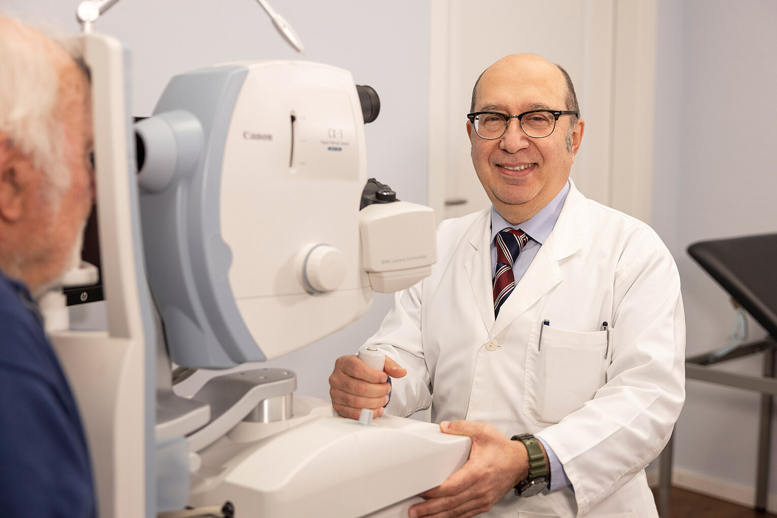 Augenarzt lächelt während ein Patient in ein Testgerät schaut.