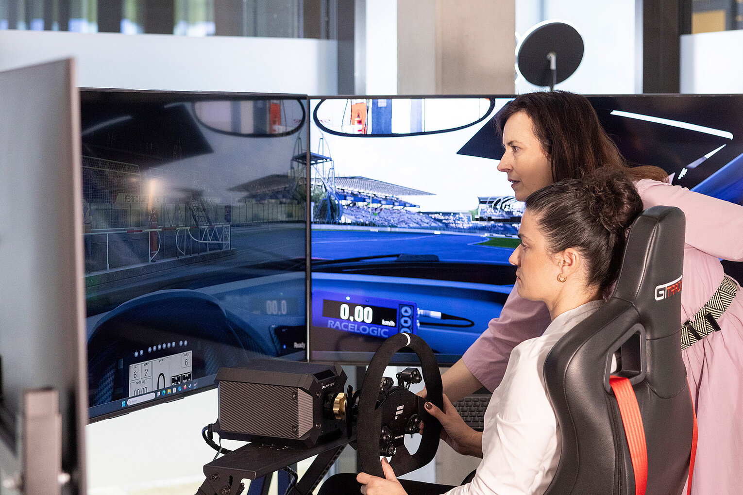 Fahrsimulation zur Erstellung eines augenärztlichen Gutachtens Zwei Frauen arbeiten gemeinsam an einem Fahrsimulator, während eine die Einstellungen überprüft und die andere fährt, um ein augenärztliches Gutachten zu erstellen.