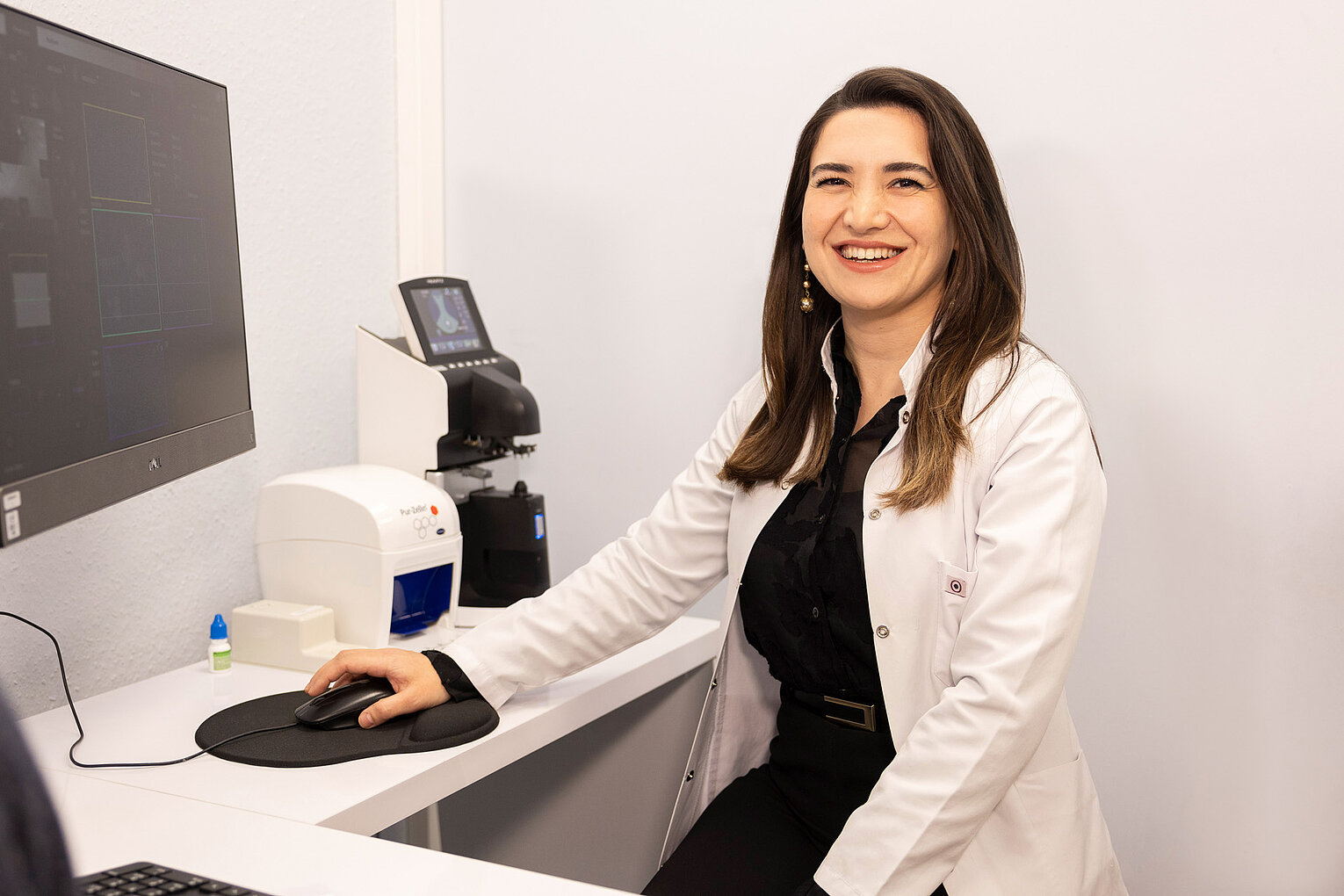 Dr. med. Leyla Guliyeva bei der Arbeit am Computer Dr. med. Leyla Guliyeva in weißem Kittel sitzt an einem Computer und zeigt auf den Bildschirm, der medizinische Daten anzeigt.