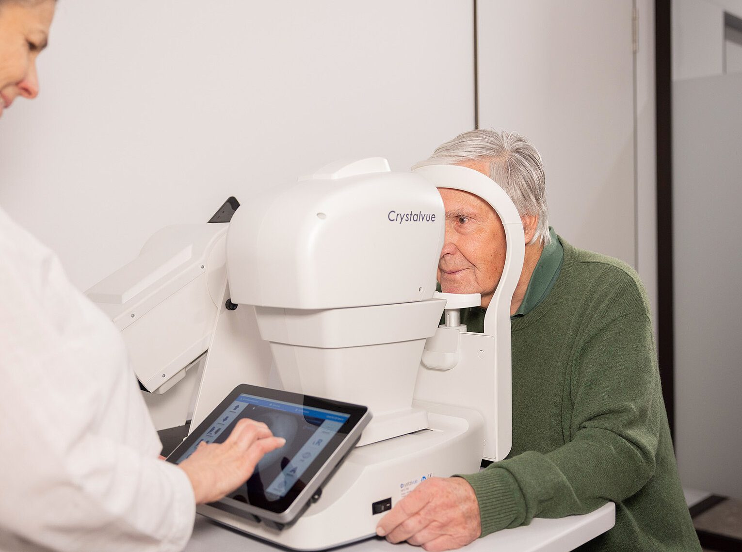 Präzise Augendiagnostik in der Praxis Ein älterer Mann schaut in ein modernes Augenmessgerät, während eine Fachkraft die Untersuchung überwacht.