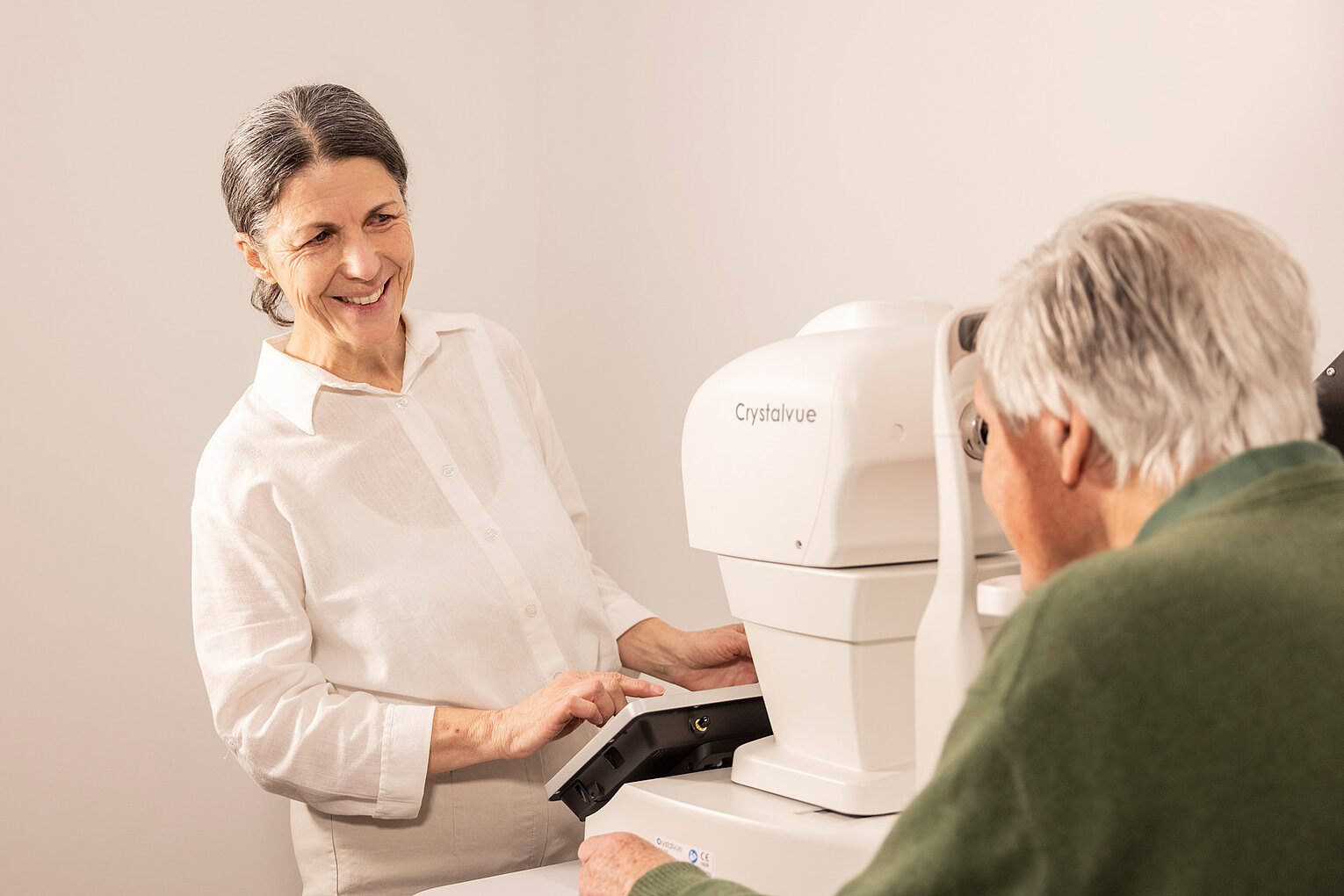 Eine freundliche Macuria Mitarbeiterin erklärt einem älteren Patienten die Augenuntersuchung mit einem modernen Gerät. 